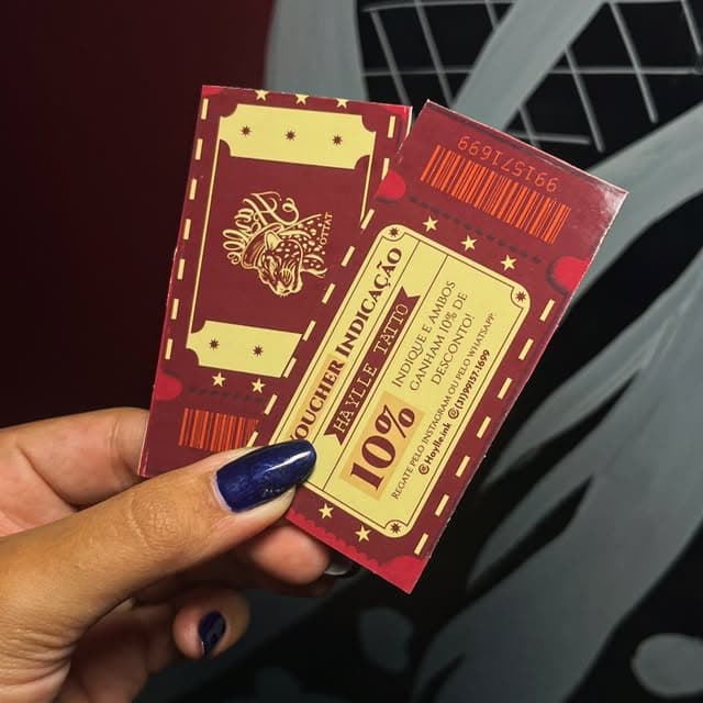 Mão segurando os tickets impressos do estúdio, um deles o voucher de indicação com 10% de desconto
